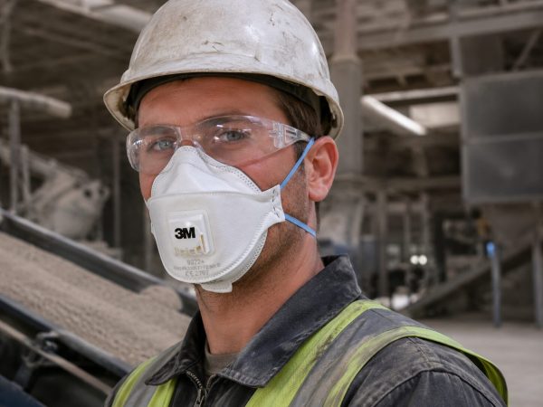 Operario utilizando mascarilla 3M Aura 9322+ FFP2 con válvula y gafas de protección en ambiente industrial con polvo