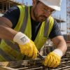Operario de construcción usando guantes de seguridad NITREX amarillos mientras trabaja con ferralla en una obra.