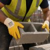 Albañil sujetando un bloque de hormigón con guantes amarillos NITREX 230 en una obra de construcción.
