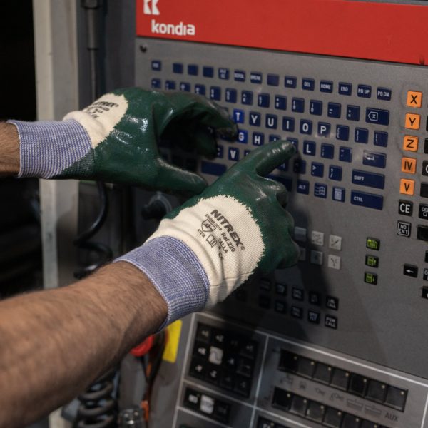 Trabajador con guantes NITREX 220 recubiertos de nitrilo utilizando un panel de control industrial en fábrica.
