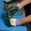 Operario usando guantes de seguridad NITREX 220 mientras ajusta una pieza metálica en maquinaria industrial azul.