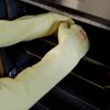 Panadero utilizando el guante térmico largo NITREX 285L para extraer bandejas calientes del horno industrial
