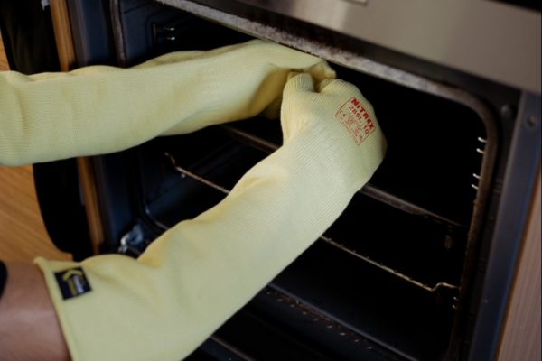 Panadero utilizando el guante térmico largo NITREX 285L para extraer bandejas calientes del horno industrial