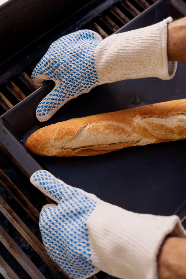 Operario utilizando guantes NITREX 281 anti-calóricos con puntos de nitrilo para manipular bandejas calientes de pan en horno industrial