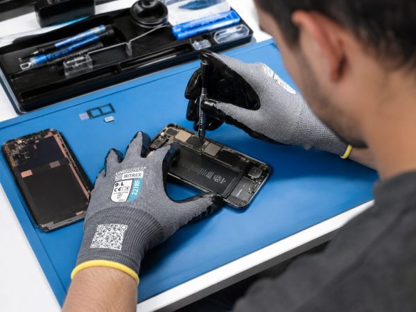 Técnico realizando reparación de smartphone con guantes anticorte Nitrex 221RF de alta precisión y compatibilidad táctil.