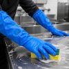Operario utilizando guantes largos NITREX 314LNIT azules durante la limpieza de una superficie industrial con espuma y productos de limpieza.