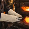 Trabajador utilizando guantes térmicos largos NITREX 280 para manipular metal caliente en entorno industrial de alta temperatura