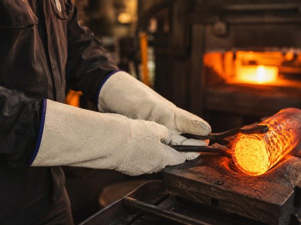 Trabajador utilizando guantes térmicos largos NITREX 280 para manipular metal caliente en entorno industrial de alta temperatura