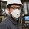 Operario con casco y gafas de seguridad utilizando mascarilla 3M Aura 9332 Gen3 FFP2 con válvula en fábrica industrial