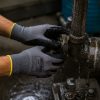 Trabajador apretando manualmente una tuerca en una tubería industrial mojada con guante nitrex 250