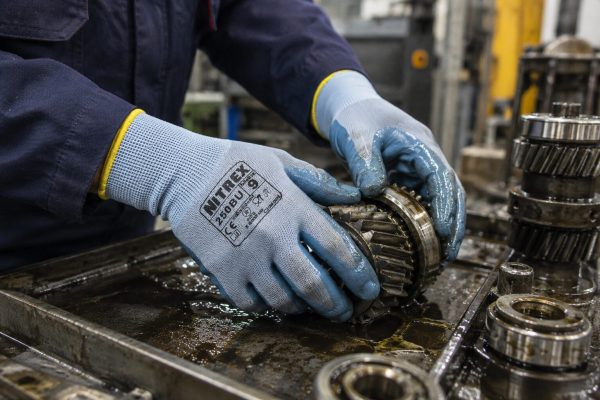 Trabajador sujetando engranajes metálicos aceitosos con guantes NITREX 250BU.