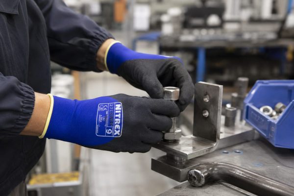 Operario trabajando con maquinaria industrial usando guantes NITREX 270NFP.