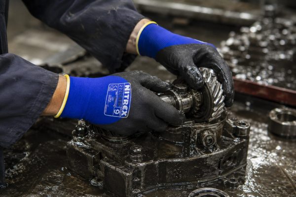 Trabajador manipulando engranajes aceitosos con guantes NITREX 270NFP.