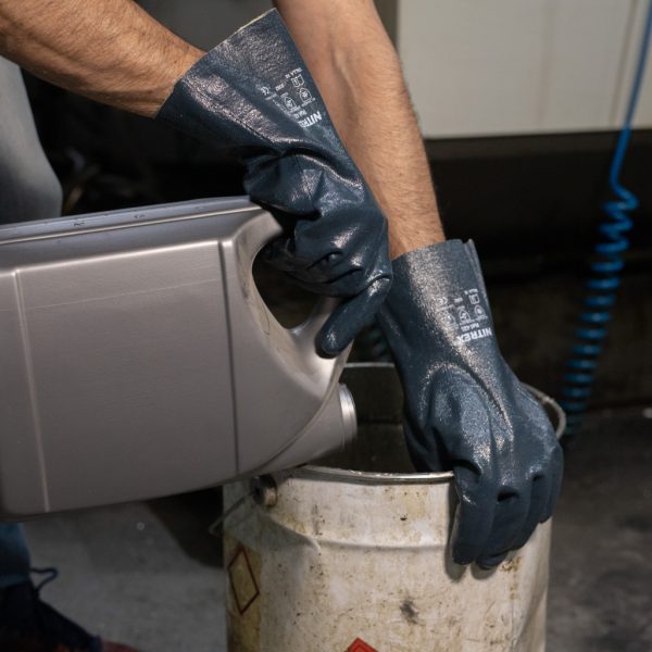Operario utilizando guantes de nitrilo azul Nitrex 420 para manipular productos químicos y aceites en un bidón.
