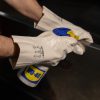 Operario con guantes de nitrilo blanco Nitrex 420BL aplicando espray lubricante WD-40 en una superficie metálica.